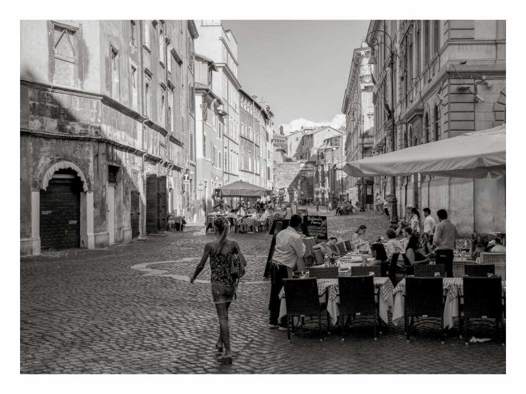 Roman Piazza print, 123.5 × 90 cm with white border — cobblestone piazza with a café terrace and figures walking past historic buildings, Rome, Italy, black and white street photography by Tom Parsons