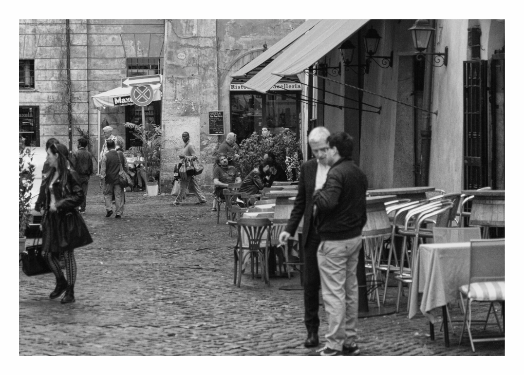 Street Handbag Seller print, 129.8 x 90 cm with white border — man carrying knock-off handbags through a Trastevere piazza, Rome, black and white street photography by Tom Parsons