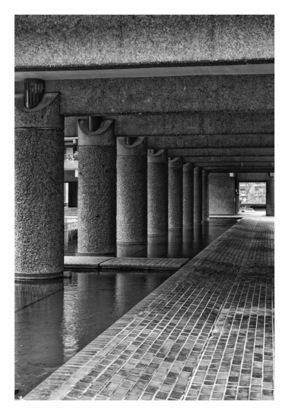 Barbican print, 90 × 133.6 cm with white border — colonnaded walkway beside water at the Barbican Centre, London, black and white architecture photography by Tom Parsons