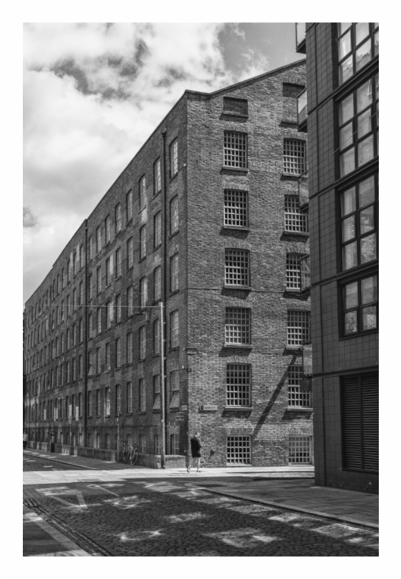 Street in Manchester print, 80 × 120 cm with white border — Victorian brick warehouse on a cobbled Manchester street corner, lone pedestrian, black and white street photography by Tom Parsons