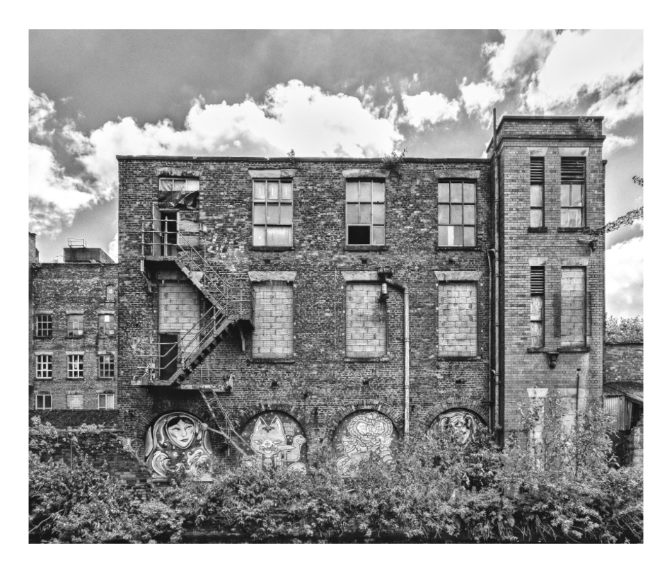 Manchester canal warehouse print, 107.5 × 90 cm with white border — weathered brick canal warehouse with a fire escape and street art murals, Manchester, black and white architecture photography by Tom Parsons