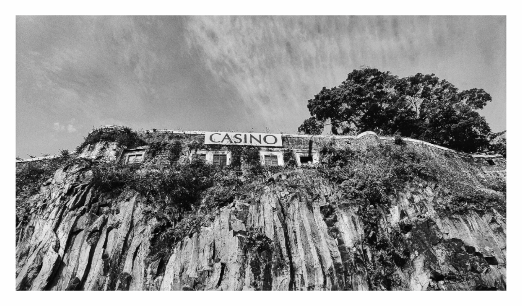 Casino print, 160 × 90 cm with white border — abandoned casino with a faded sign, perched on a volcanic cliff above the harbour, Madeira, black and white architecture photography by Tom Parsons