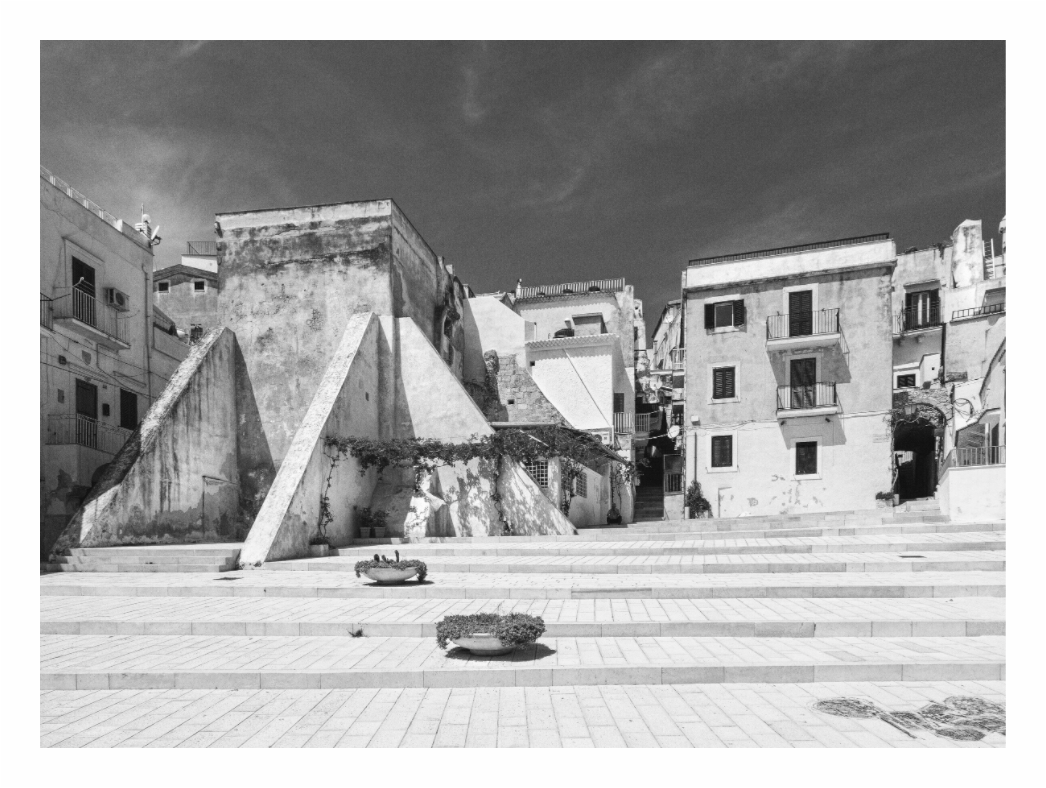Town square print, 122.8 × 90 cm with white border — empty piazza with triangular stone stairs and weathered buildings, Puglia, Italy, black and white street photography by Tom Parsons