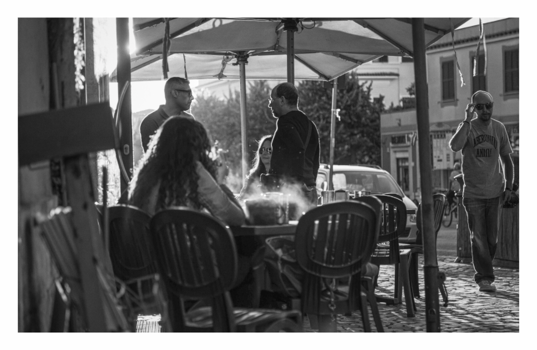 Street scene, Cafe print, 143.1 × 90 cm with white border — people gathered at an outdoor café table, Ostia Antica, Rome, black and white street photography by Tom Parsons